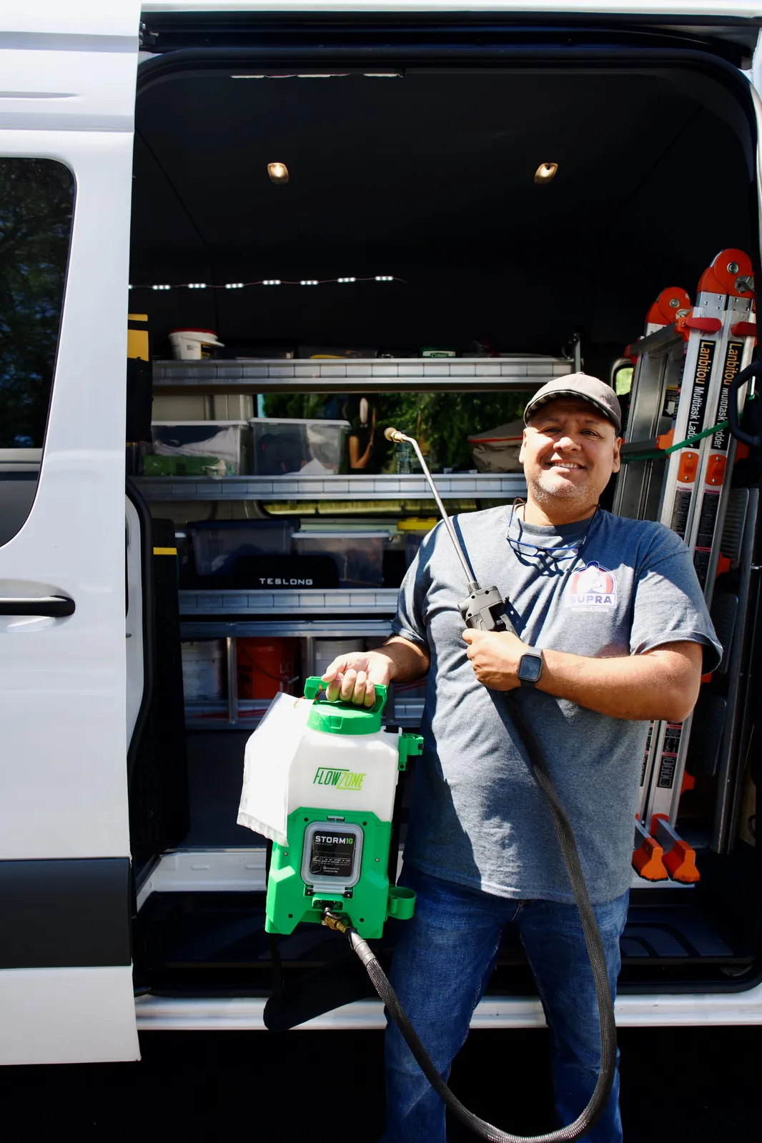 Supra Exterminator technician holding a backpack sprayer at the open door of a service van